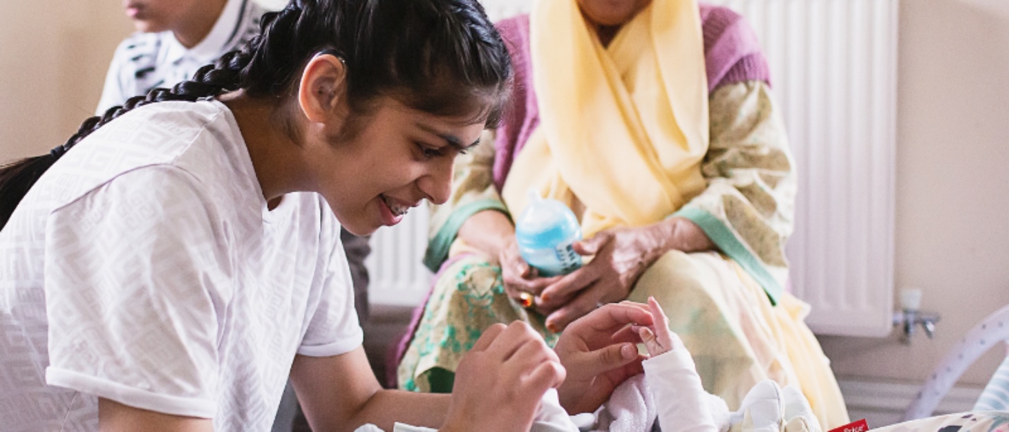 a girl playing with her baby sister while their brother and grandma look over them