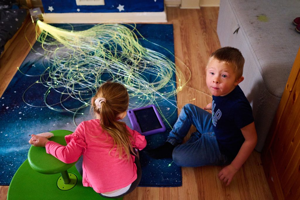 A brother and sister sit in their room playing with fibre optic sensory lights. 