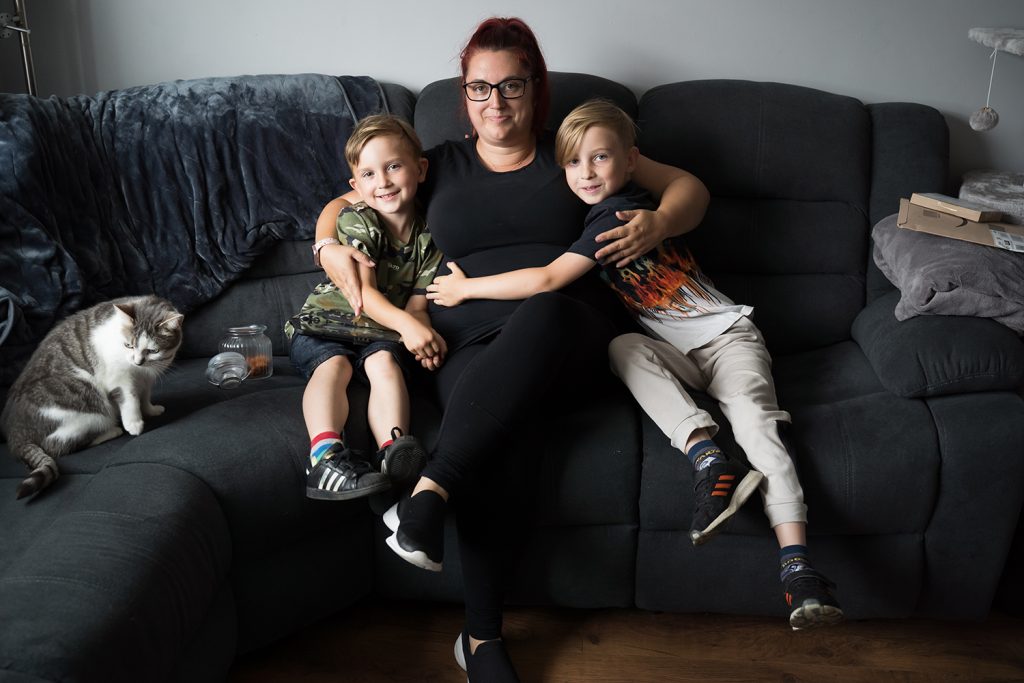 Mum sits on the sofa hugging her two sons either side of her. 