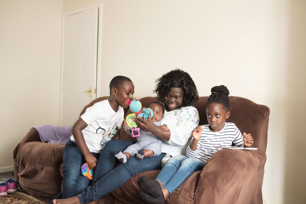 a mum and her three children sitting on a couch, playing and reading a book together