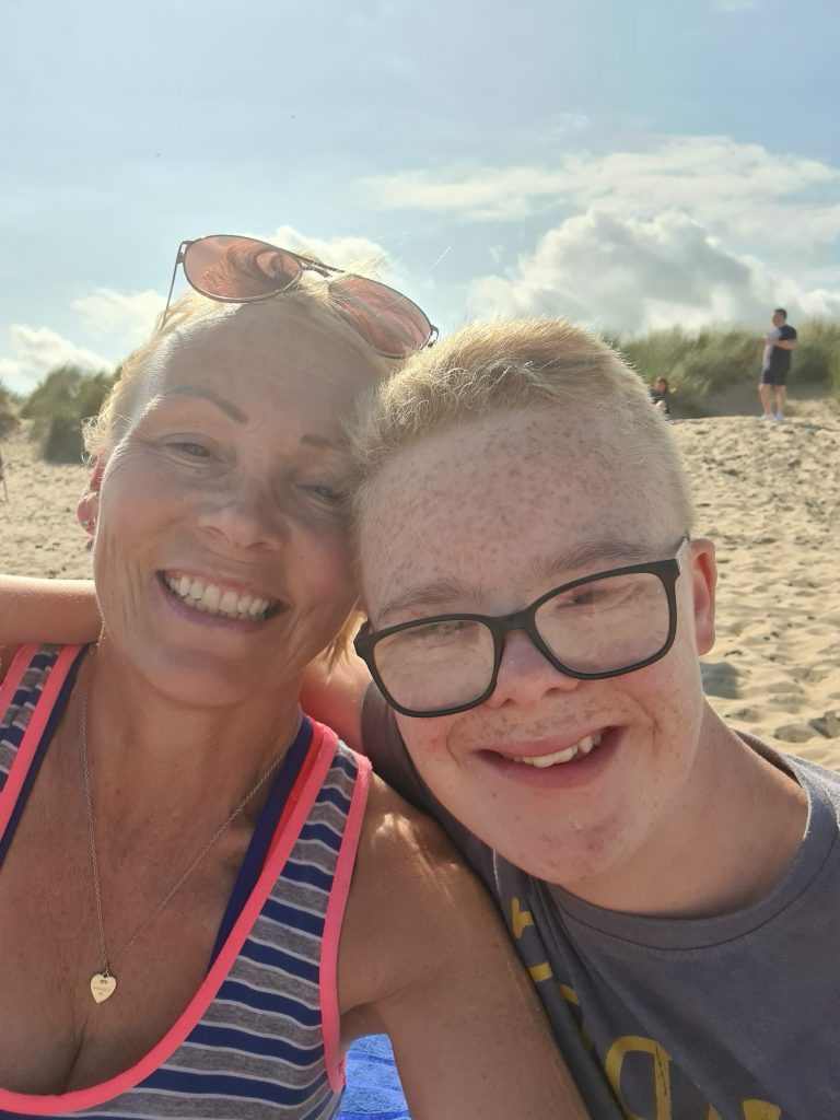 Son hugs mum on beach on sunny day