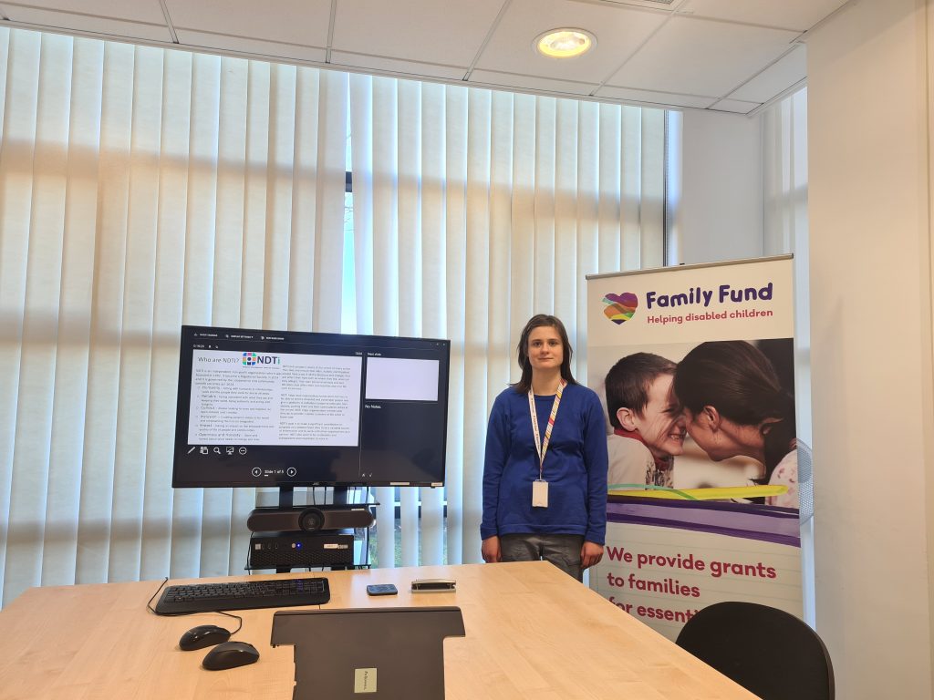 Alice, Family Fund's supported intern, stands in front of a presentation on a screen and a Family Fund banner.