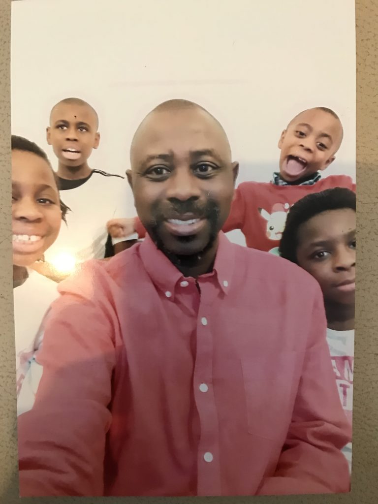 Man smiles for a selfie with his four children in the background