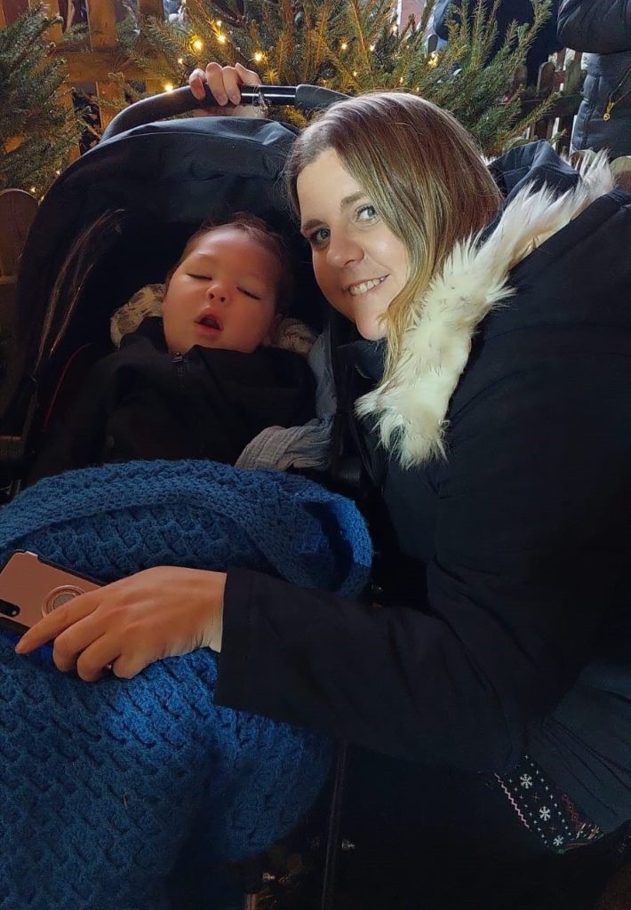 Mum crouches next to her baby who is asleep in pushchair