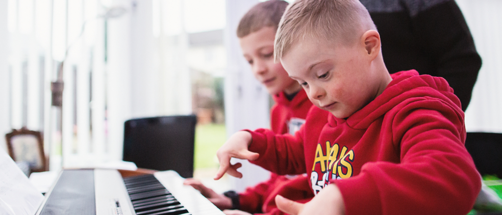 a boy wearing a red hoodie is playing the piano next to his brother and grandfather