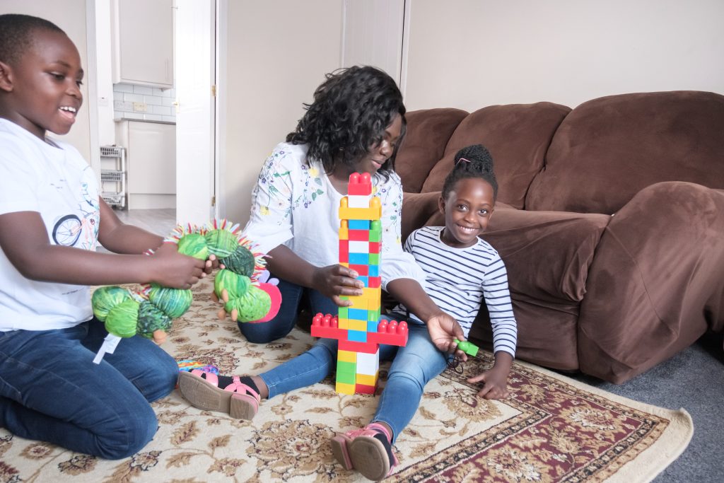 Mum sits with her son and daughter on the living room floor playing with lego