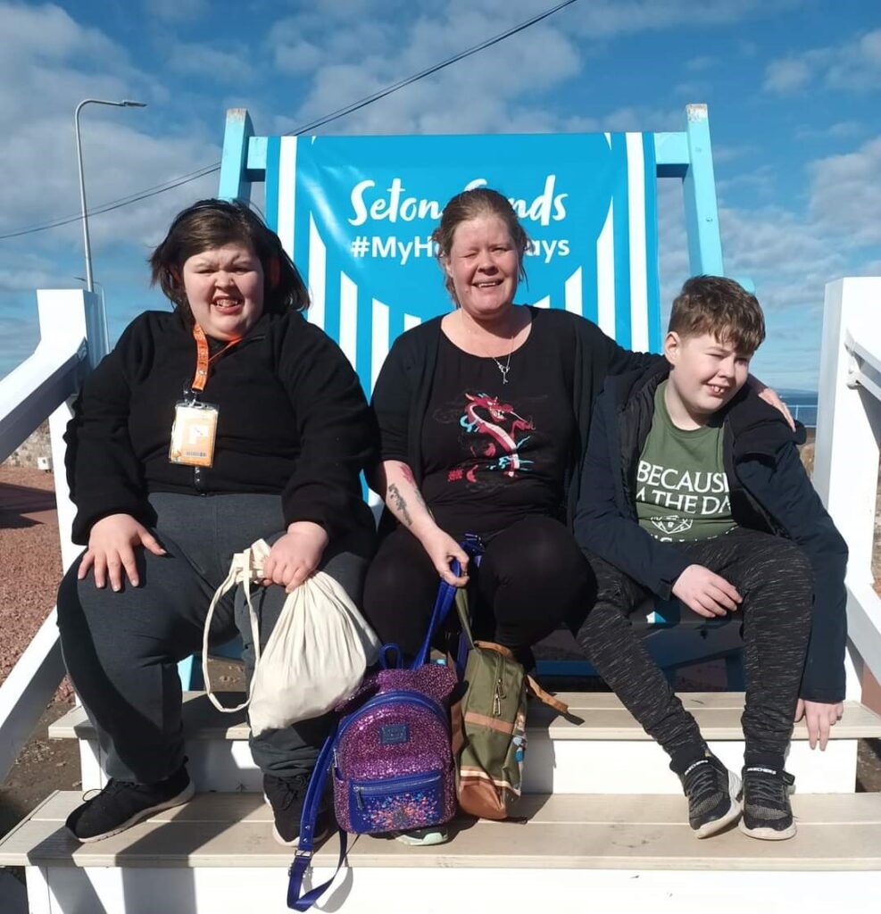 A mum, a teenage daughter and a young boy are saw on a giant blue and white lounge chair, smiling at the camera