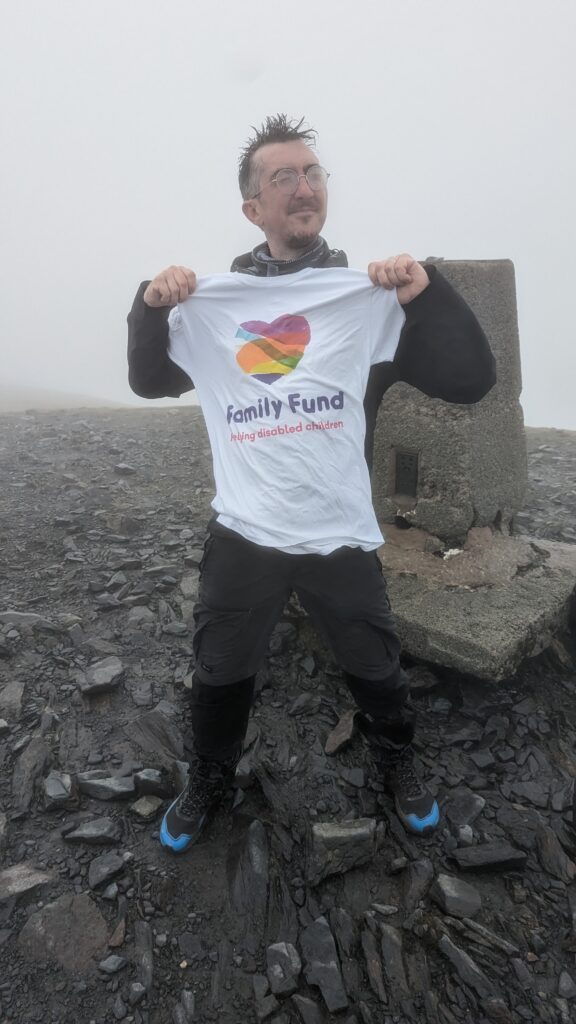 A man at the top of a foggy mountain, wearing a white tee-shirt with the family fund logo on it