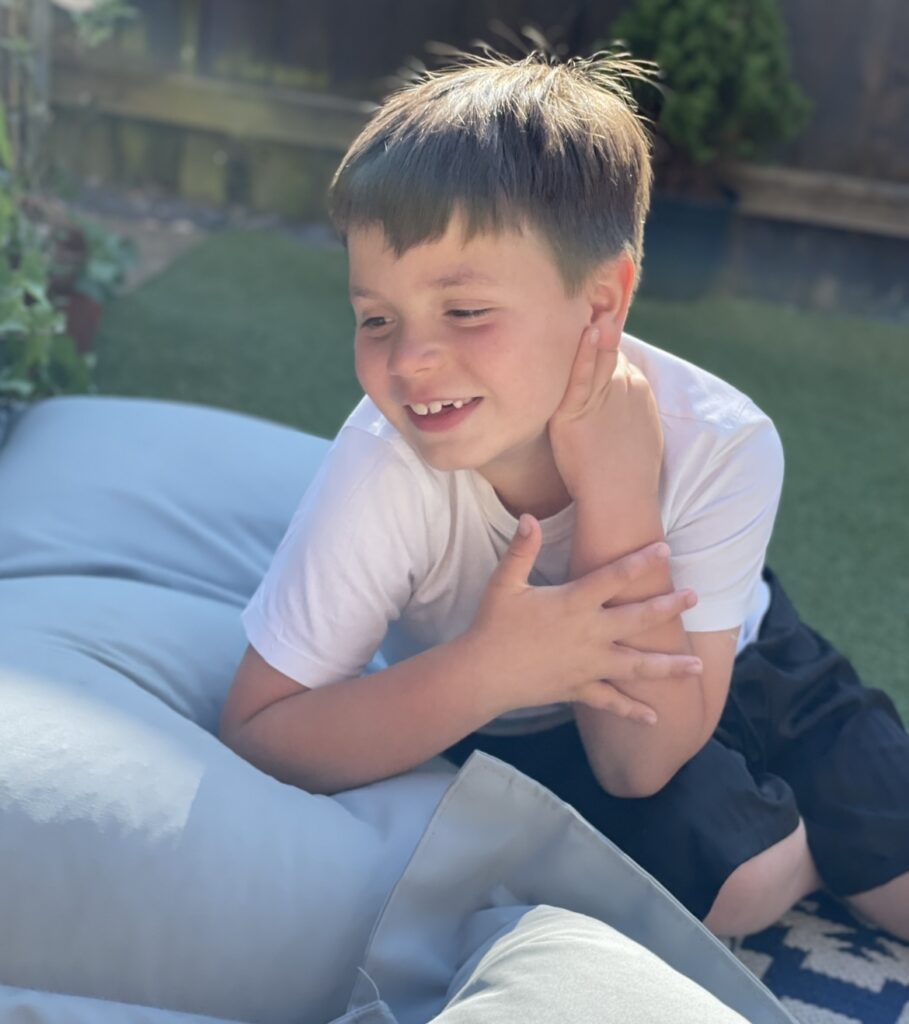 Smiling young boy with brown hair sits on bean bag in garden. 