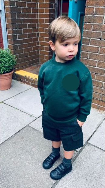 Little boy in school uniform stands outside school on his first day.