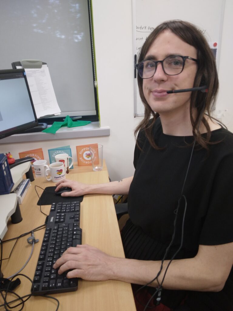 Family Fund IT Support Officer sat at her desk with a headset on in an office with her hands on the keyboard