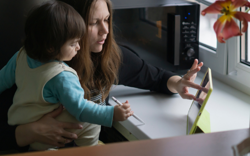 A mum is checking something on her iPad. She holds her young son in one arm