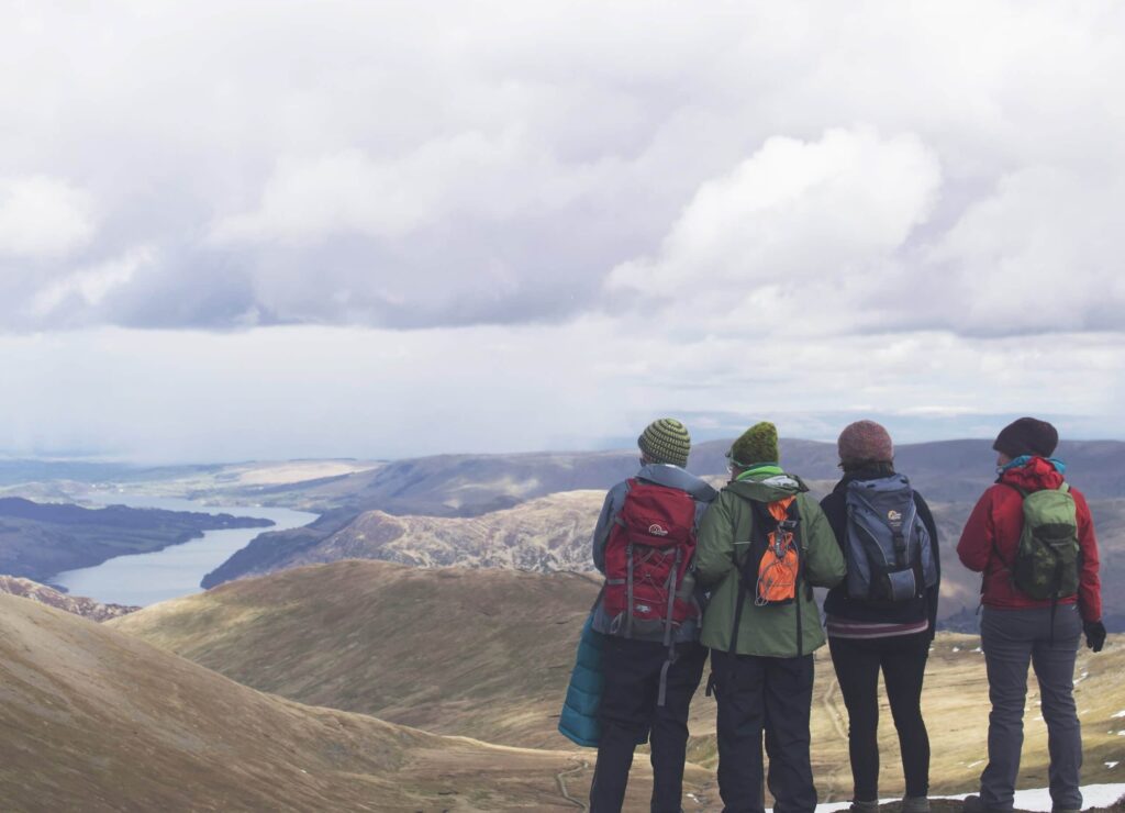 A group of four people in coats and hats stood at the top of a mountain looking at the views below