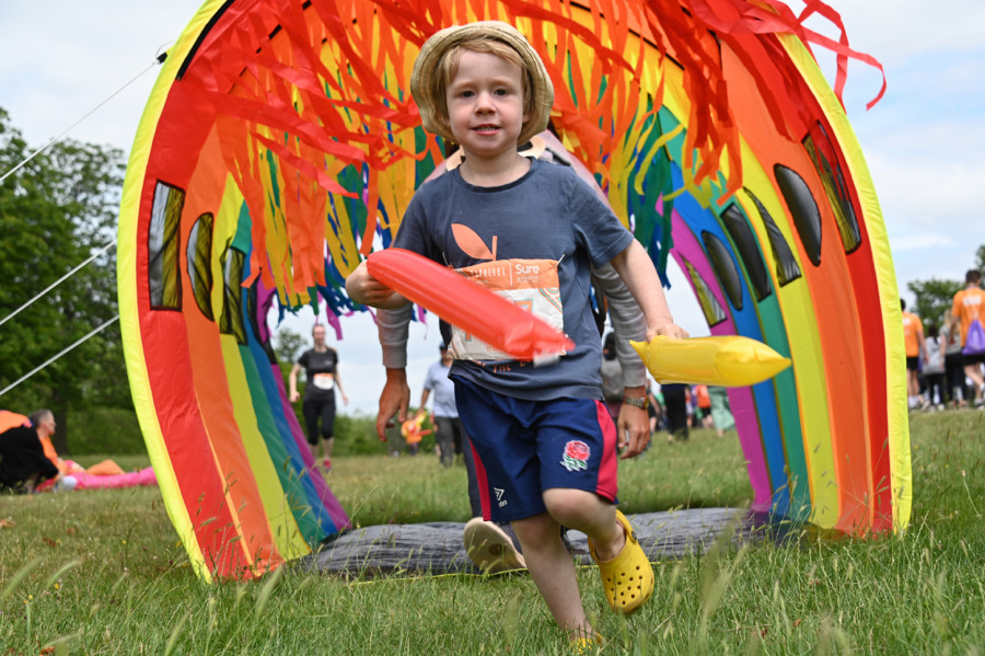A young boy in a park is playing in a colourful rainbow tunnel
