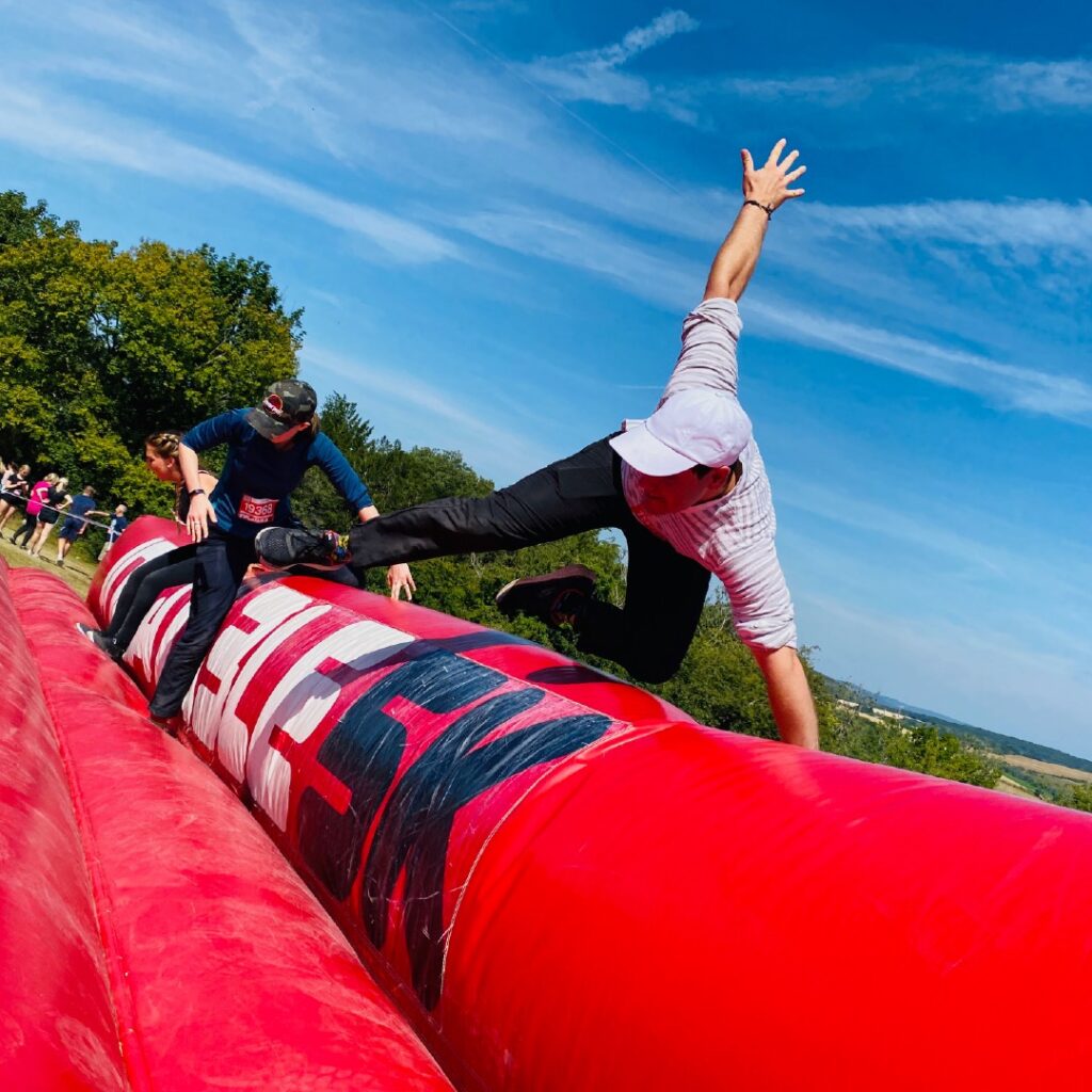 A man wearing a cap jumping over a large red inflatable wall on a sunny day