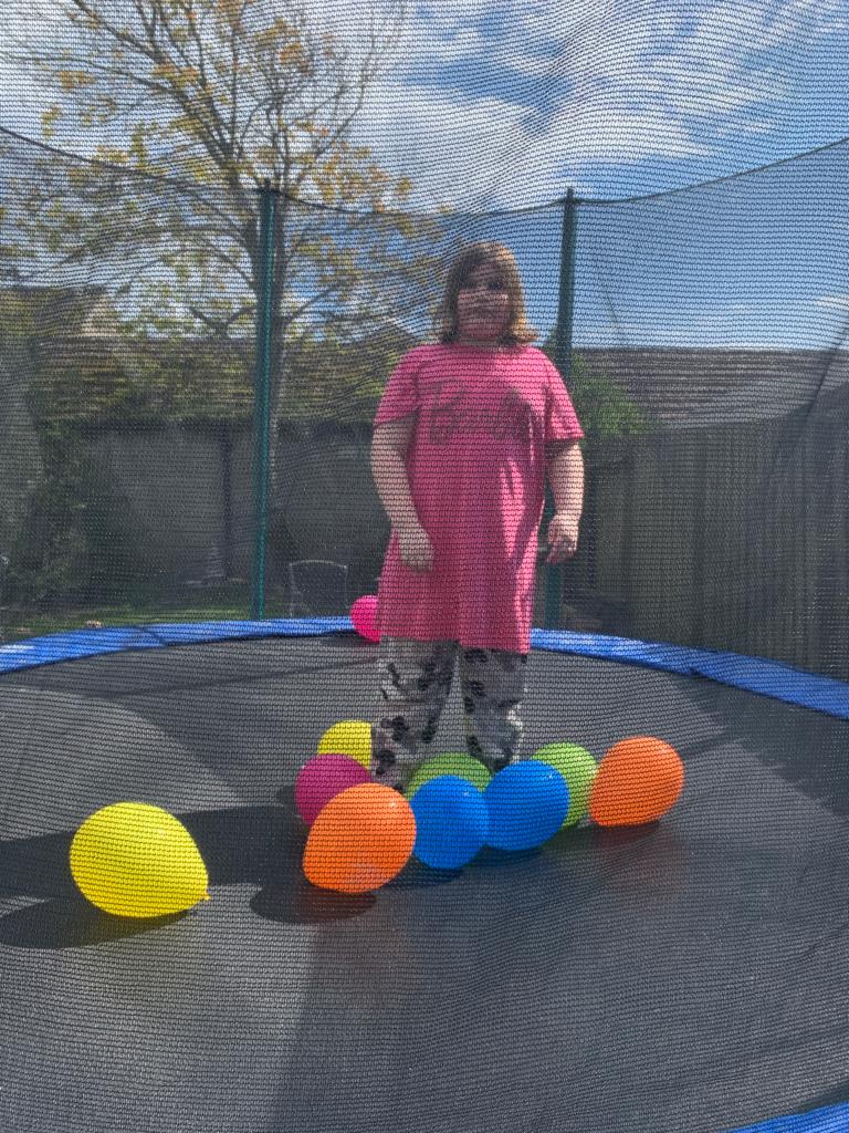 Ophelia, a 13-year-old girl, stands on an outdoor trampoline, surrounded by brightly coloured balloons.