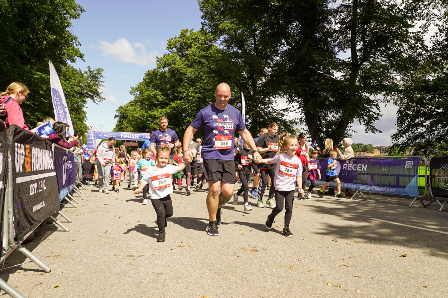 A man holds the hands of two children as they run together in the York Mini and Junior run