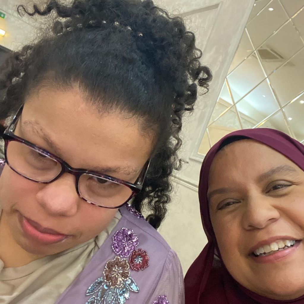 Nur, a young woman wearing glasses with her mum, Firi. Both are smiling.