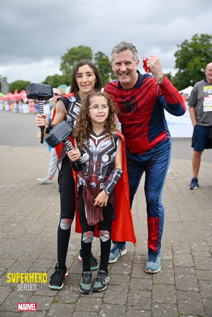 A mum, dad and child standing together in superhero outfits
