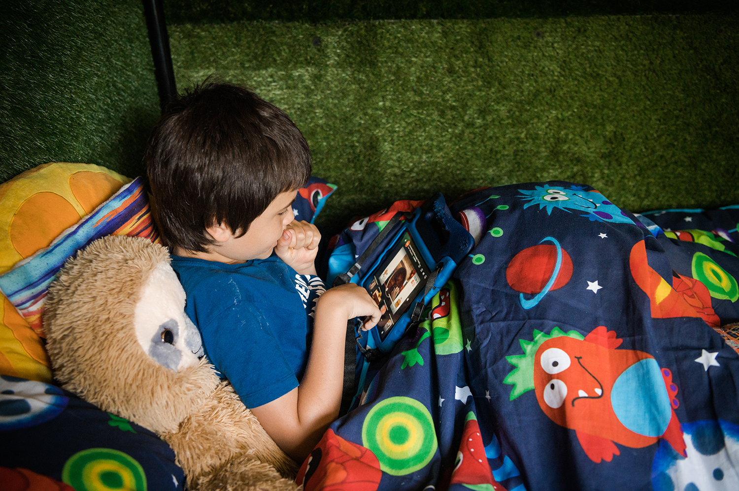 A young boy sits in bed on his tablet