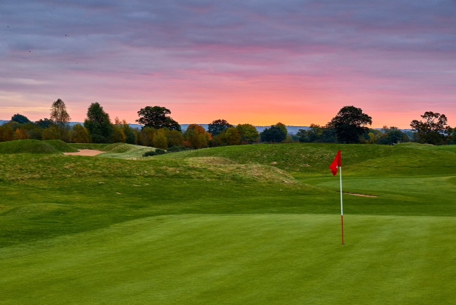 A photo of the fifth hole of the PGA National course at The Belfry. The photo has been taken at dusk with a sunset visible in the skyline.