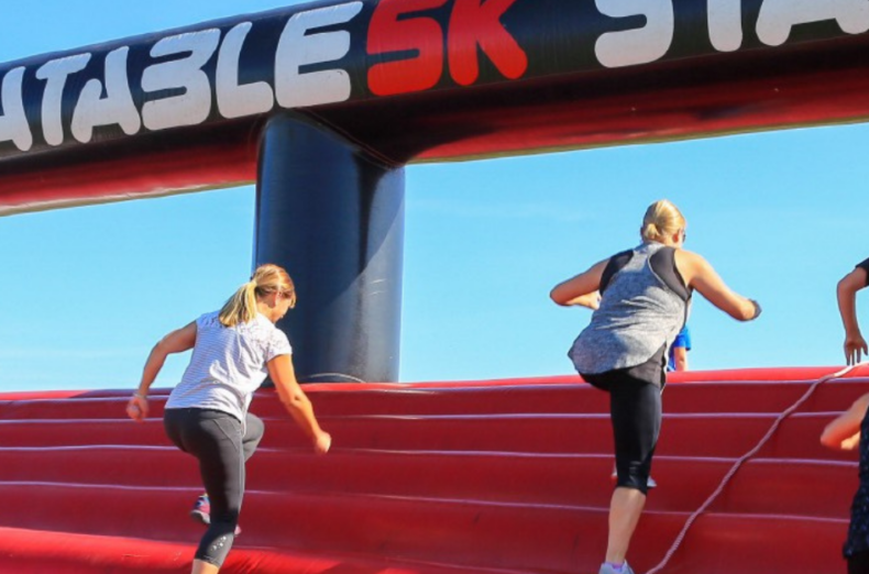 Looking up at a group of people climbing over a large red inflatable on a sunny day