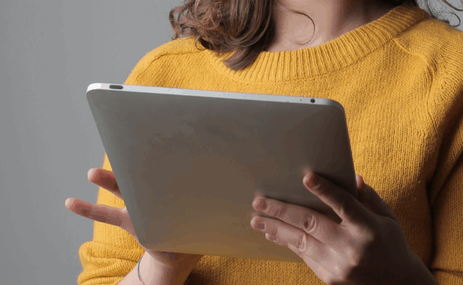 A woman wearing a yellow jumper holds an iPad in her hands