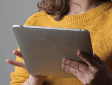 A woman wearing a yellow jumper holds an iPad in her hands