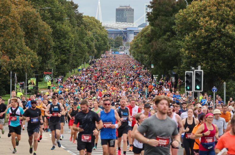 A group of people running down a tree-lined road with a city in the background.