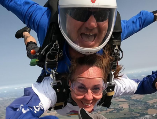 A tandem skydive in mid air, the man and woman both have their arms out smiling
