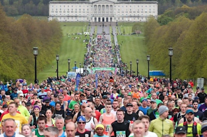 A huge crowd of people running down a load park road with a parliament building in the background