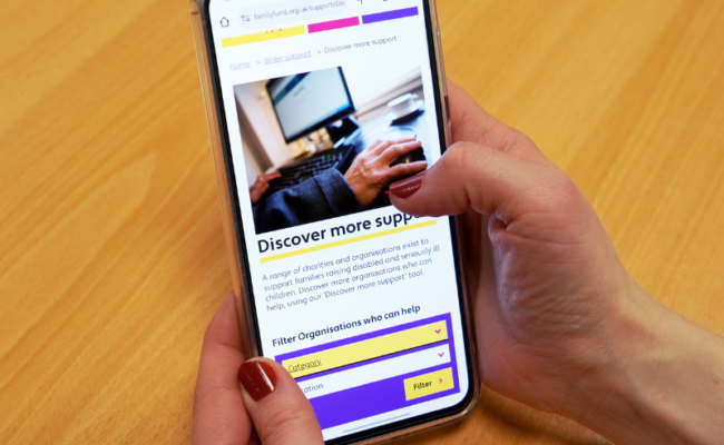A photo of two hands holding a mobile phone and browsing the Discover more support page on Family Fund website.