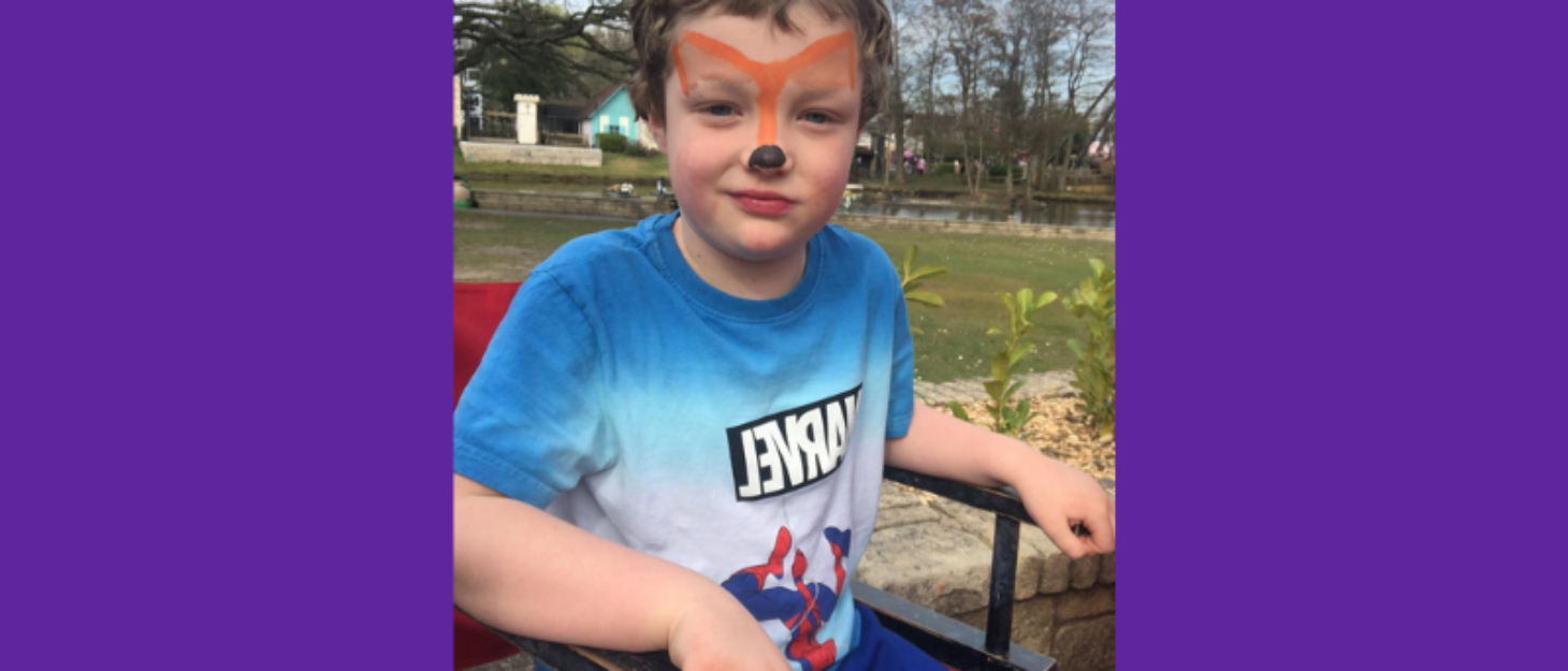 A boy sat in the chair and smiling. He has tiger face paint on.