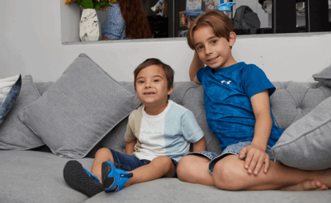 Two boys are sat on the sofa and are smiling.