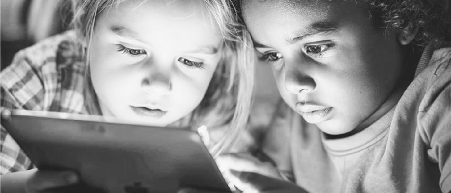 a grayscale image of 2 children looking at an ipad