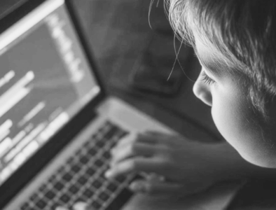 A grayscale image of a child looking at a computer