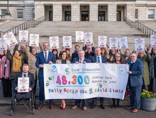 People from charities standing in front of Stormont with a banner asking the Chancellor to scrap the 2 child limit