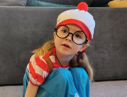 A young child crouches on the floor wearing a Where's Wally fancy dress costume