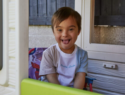 A child, smiling, sat in a toy playhouse