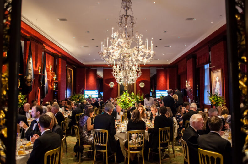 A room set up for a charity dinner at the Grocers' Hall in London. In the centre of the room is a large, ornate chandelier.