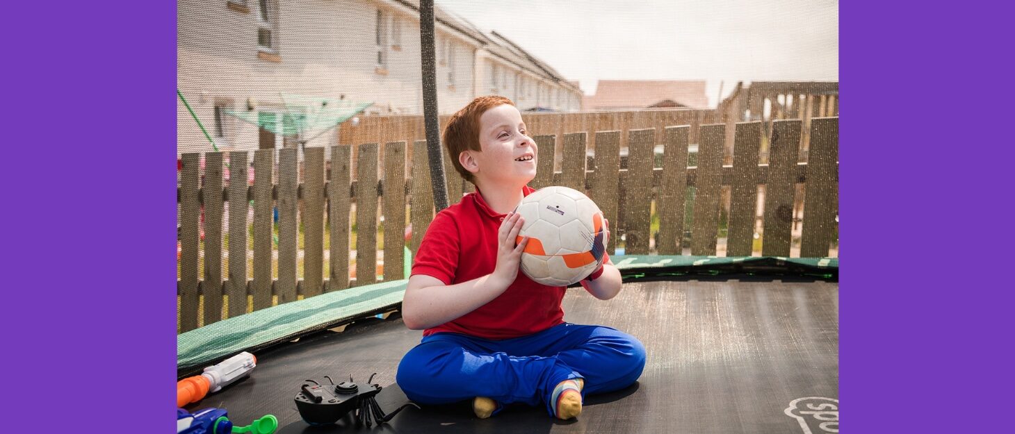 Boy sitting on trampoline about to throw a football