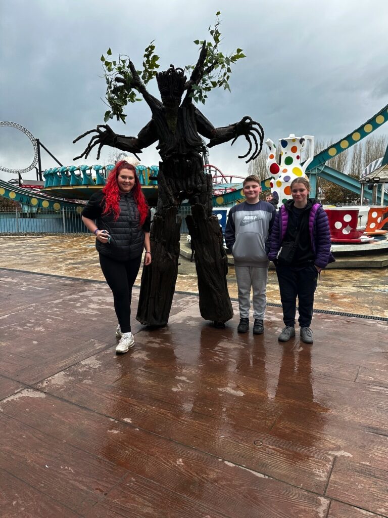 Three siblings stand in front of a sculpture of a tree and smile at the camera.