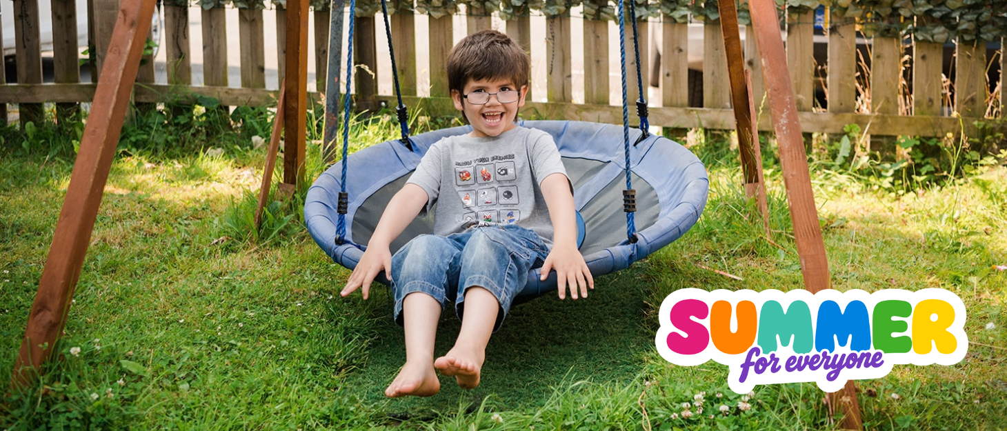 A young boy sits on a swing in his garden in the sunshine smiling. A logo in the bottom corner reads 'summer for everyone'.