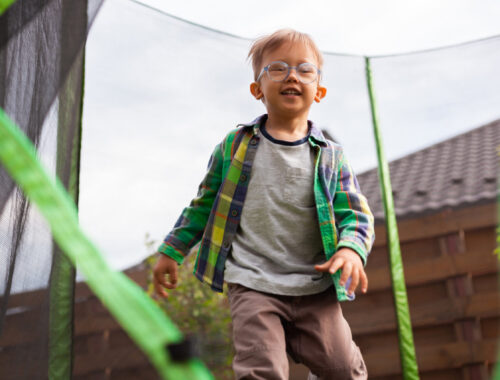 A young boy wearing glasses jumps on a trampoline