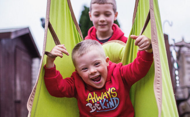 Two brothers play together in the garden on a swing.