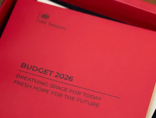 A red folder with paper inside sits on a table. Black writing on the front says "BUDGET 2026".