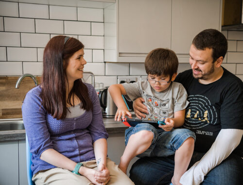 A mother and father with their son in between them, sitting in a kitchen talking