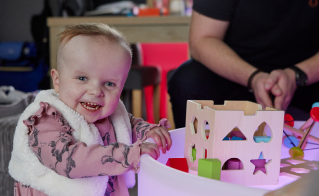 a girl in a pink dress playing with a wooden toy and laughing