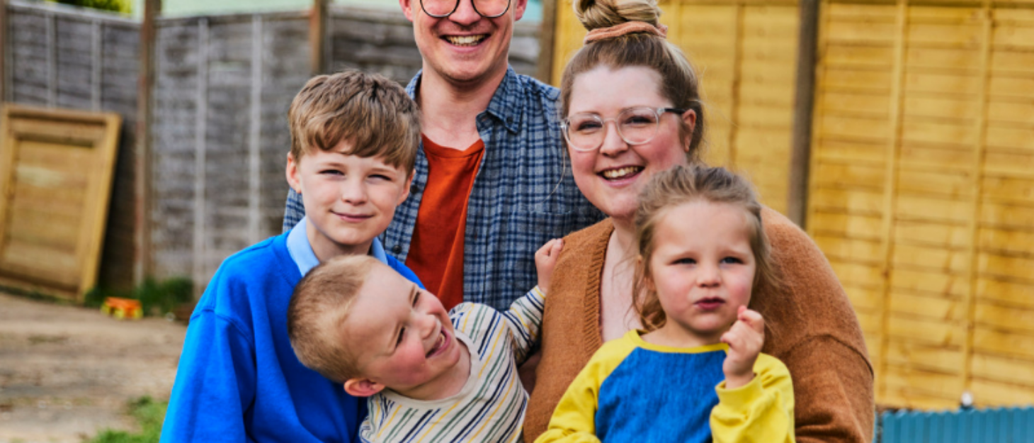 A family (mum, dad, two brothers and a sister) smile together in their garden.