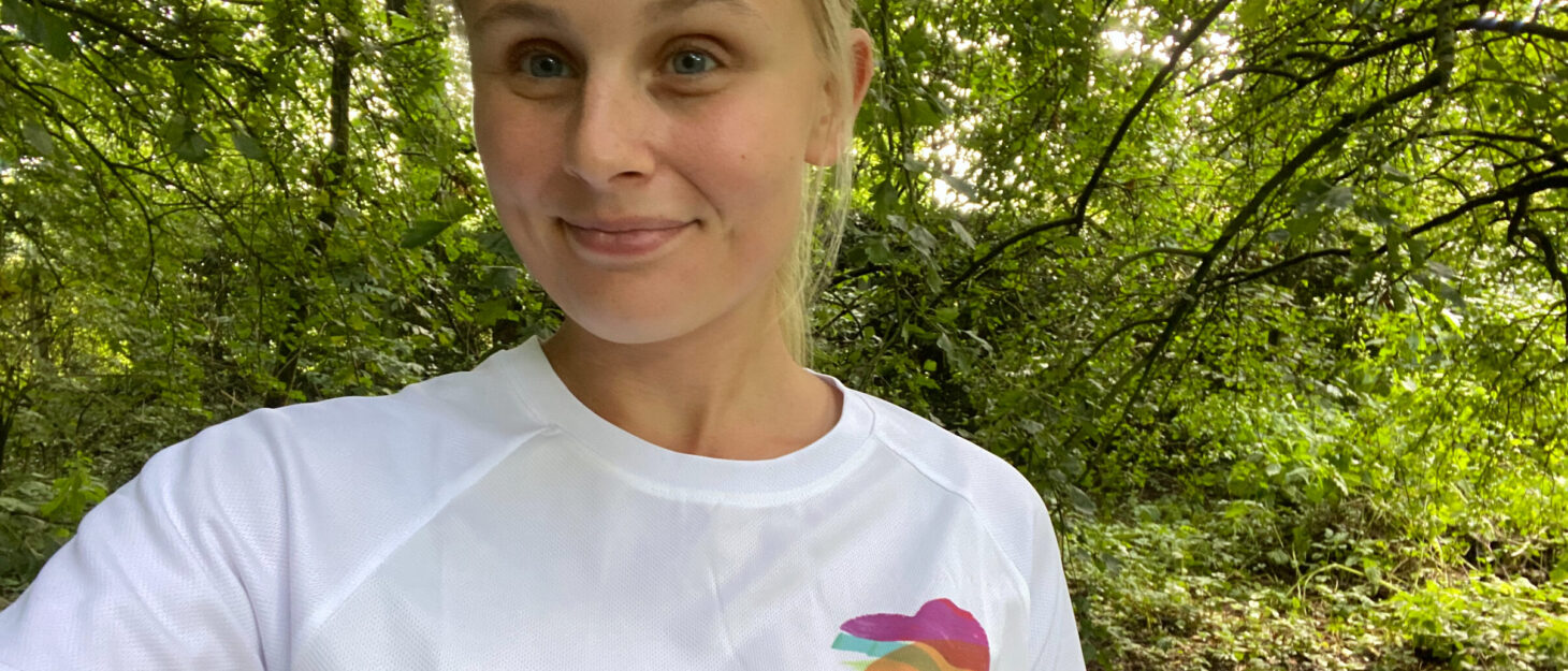 A woman in a woodland area taking a selfie wearing a white Family Fund t-shirt
